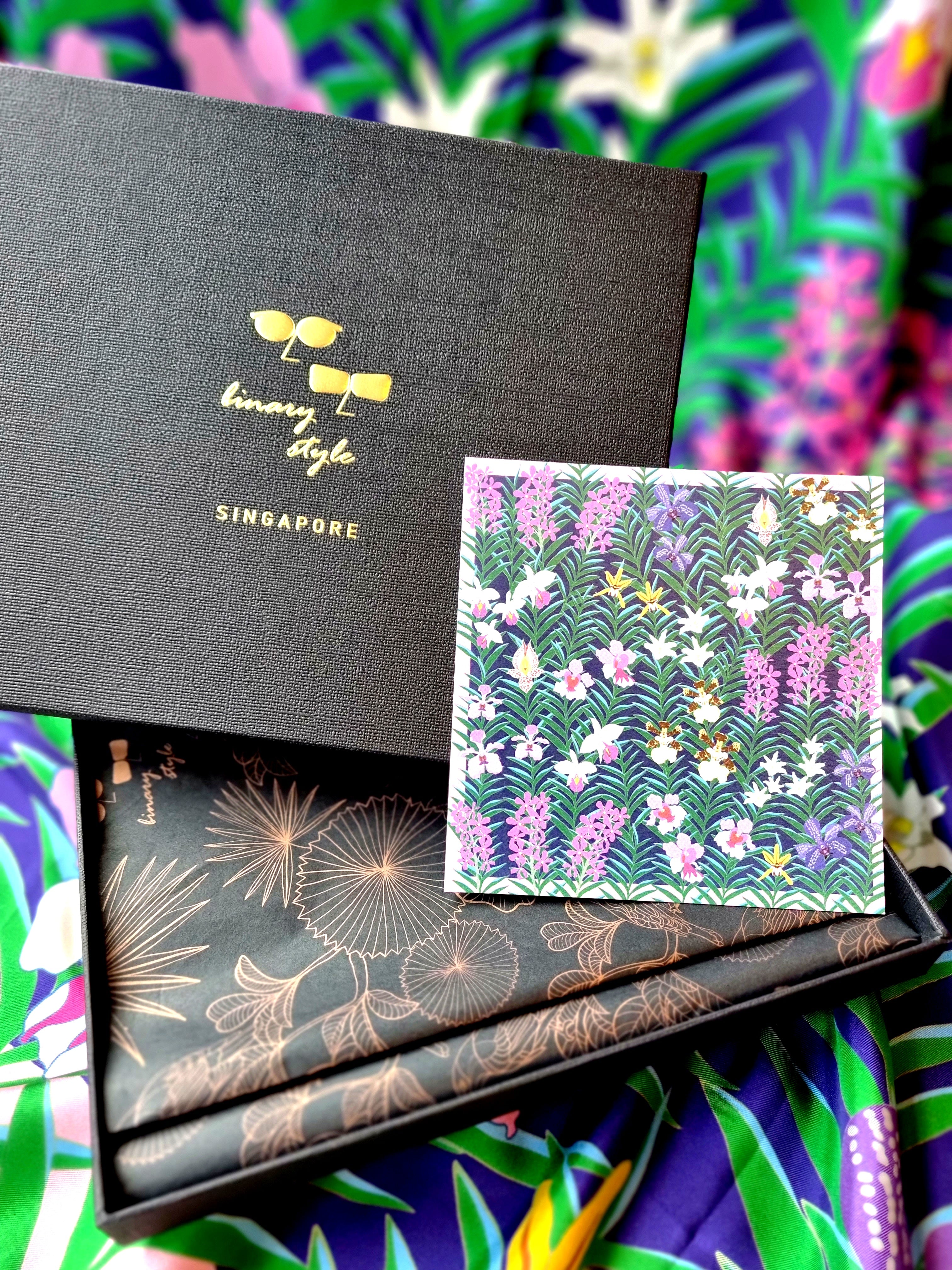 Close-up of an open black Binary Style gift box with a floral design postcard inside, on a colourful floral background